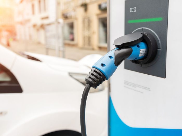 Close-up of an electric car charging station with a car in the background